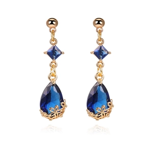Detail of 18K gold teardrop earring featuring dark blue faceted crystal and floral filigree