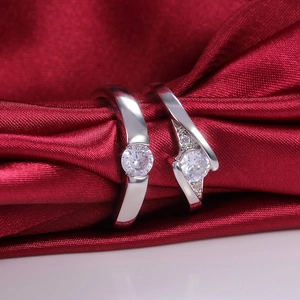Silver couple rings with round zircon stones on a luxury red satin fabric background
