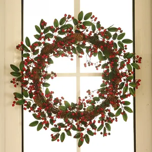Détail d'une couronne de Noël avec baies rouges, pommes de pin et feuilles sur fenêtre
