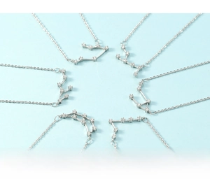 Detail of silver zodiac necklaces with sparkling zircon stones on light blue background