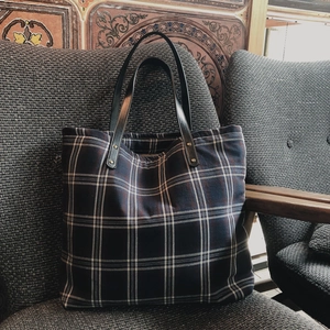 Detail of blue plaid tote bag with black leather handle and rivet on gray fabric
