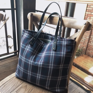 Classic red and navy plaid canvas tote bag with black leather handles on a wooden chair
