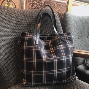 Close-up of a plaid tote bag with vintage checks and leather handles on a grey sofa