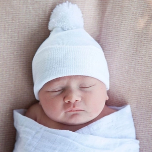 Close-up of a soft white newborn knitted beanie with a pom-pom on a sleeping baby