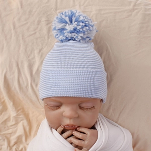 Detail view of soft blue striped newborn knit hat with fluffy pom-pom on doll model