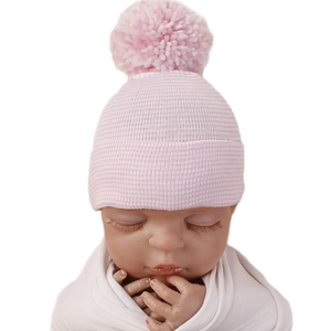 Pink double-layered knitted newborn beanie with pom-pom on a baby model