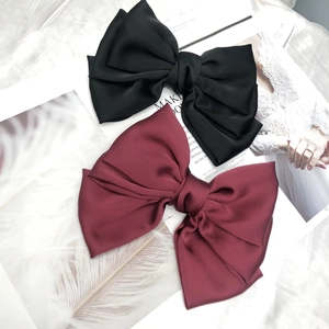 Detail of burgundy and black oversized satin bow hair clips with silky texture and sheen