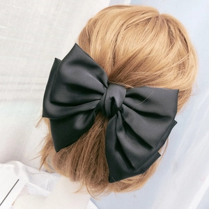 Macro detail of a large black satin bow hair clip on long golden brown hair