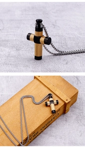 Detailansicht eines schwarz-goldenen Kreuzanhängers mit Edelstahlkette auf einer Holzbox