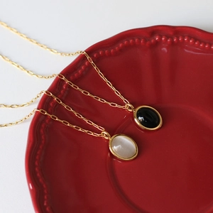 Detail of vintage 18K gold-plated oval opal and onyx pendants on a red ceramic plate