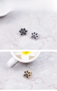 Macro view of crystal paw print stud earrings in silver and gold finishes
