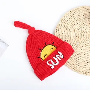Close-up of red ribbed knit beanie with sun embroidery and yellow top knot detail