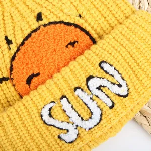Close-up of yellow knit beanie featuring orange sun pattern and white SUN embroidery