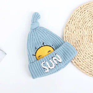 Close-up of sky blue knitted baby hat with yellow sun embroidery and top knot detail