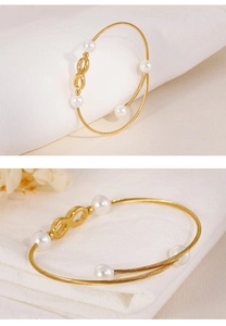 Detail van gouden gedraaide armband met witte parels en een oneindigheidssymbool