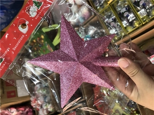 Close-up of pink glitter Christmas tree star topper in clear packaging with red header