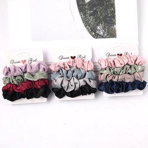 Close-up of three sets of colorful satin scrunchies displayed on branded white cards