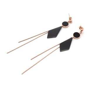 Close-up of rose gold tassel earrings with black geometric diamond and circle charms