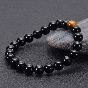 Detailed close-up of glossy black onyx beads and a brown tiger eye stone on a textured surface