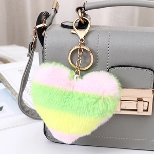 Close-up of heart-shaped plush keychain with pink green yellow stripes on a grey bag