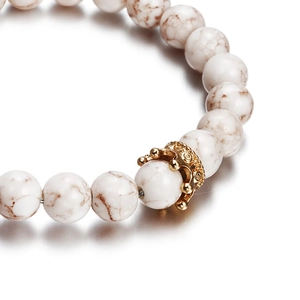 Macro shot of white marbled stone beads and a detailed golden crown charm on the bracelet