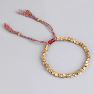 Detalle de la pulsera artesanal de cordón rojo con cuentas doradas y borlas de colores