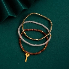 Detail of three-piece beaded necklace set with golden key charm on a green background
