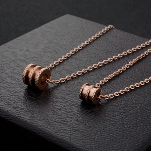 Collier en titane or rose avec pendentif cylindre strié sur une surface noire texturée