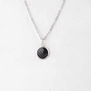 Macro view of mirror-polished stainless steel round pendant with black fish scale texture