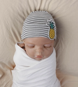 Detail of grey striped baby knit hat featuring a colorful pineapple embroidery patch
