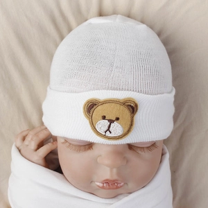 Detailed knit texture of white baby beanie featuring cute brown bear embroidery