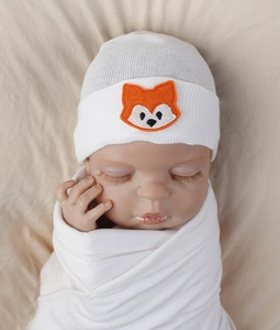 Close-up of white knitted baby hat with cute orange fox embroidery and matching swaddle