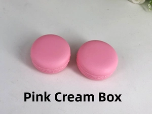 Top view of two pink macaron shaped cream jars for cosmetic storage on a grey surface