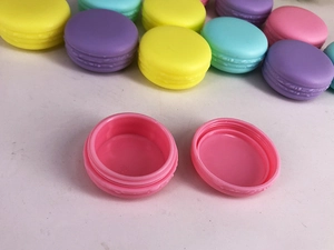 Detail of pink macaron cosmetic container with various colored plastic jars in background