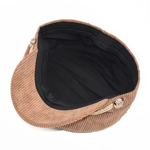 Detail of brown corduroy newsboy cap showing texture, gold rope trim, and side buttons