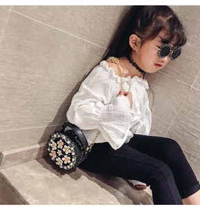 Detail of round black girls' shoulder bag with floral and pearl accents on model