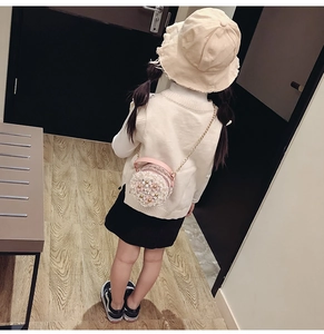 Close-up of pink round crossbody bag with floral pearls and golden chain on child model