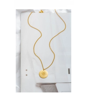 Detail of gold stainless steel sunburst evil eye necklace on white magazine background
