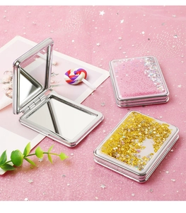 Detail of square double-sided makeup mirrors with pink and gold glitter covers on pink fabric