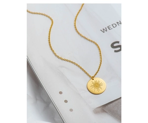 Detail shot of a gold round sunburst evil eye pendant necklace on a textile background