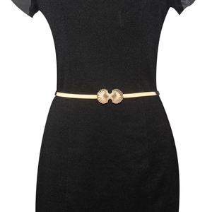 Close-up of golden shell buckle on elastic metal belt paired with a black dress
