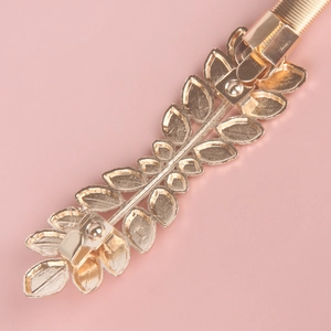 Detailed view of golden leaf-shaped metal buckle with elastic spring band for dresses