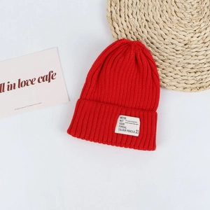 Detail of red ribbed knit beanie featuring a white rectangular patch with decorative text