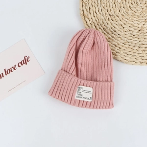 Detail of pink knitted beanie featuring a ribbed texture and white woven label patch