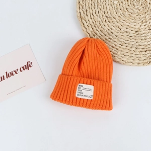 Detail of bright orange knitted beanie with a square white patch on white background