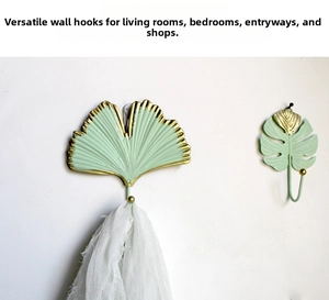 Wall hooks featuring mint green and gold ginkgo and monstera leaf shapes on white wall