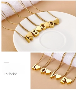 Detailed macro view of gold heart and letter pendants on a delicate box chain necklace