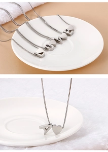 Macro detail of titanium steel necklace with 3D letters and heart charms on a box chain