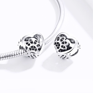 Macro shot of silver heart charms with black paw print patterns on a snake chain bracelet