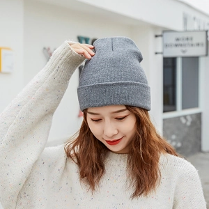 Detail of grey knitted beanie with colored flecks worn by a model in outdoor street setting